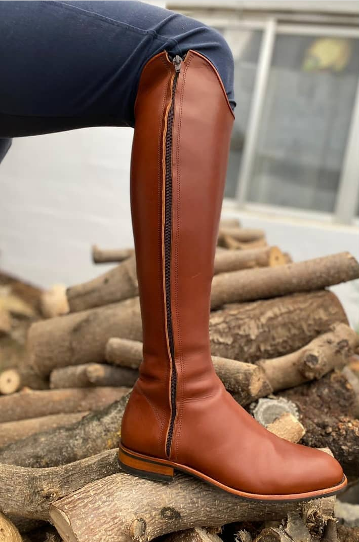 Bota alta castanha em pele com fecho preto ao lado sobre troncos de madeira