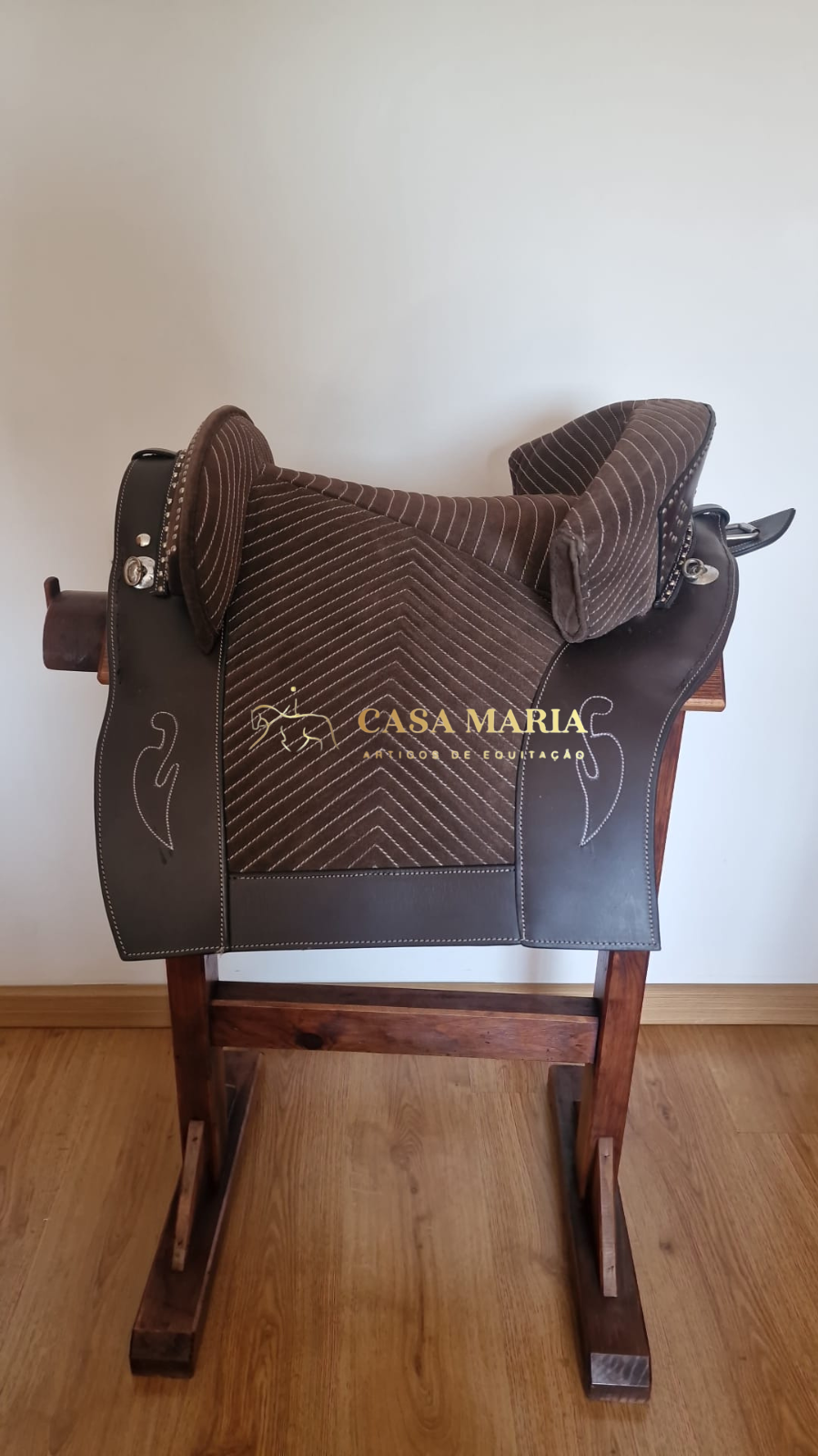 Selim de equitação castanho escuro em suporte de madeira com texto CASA MARIA AMOR DE EQUITAÇÃO