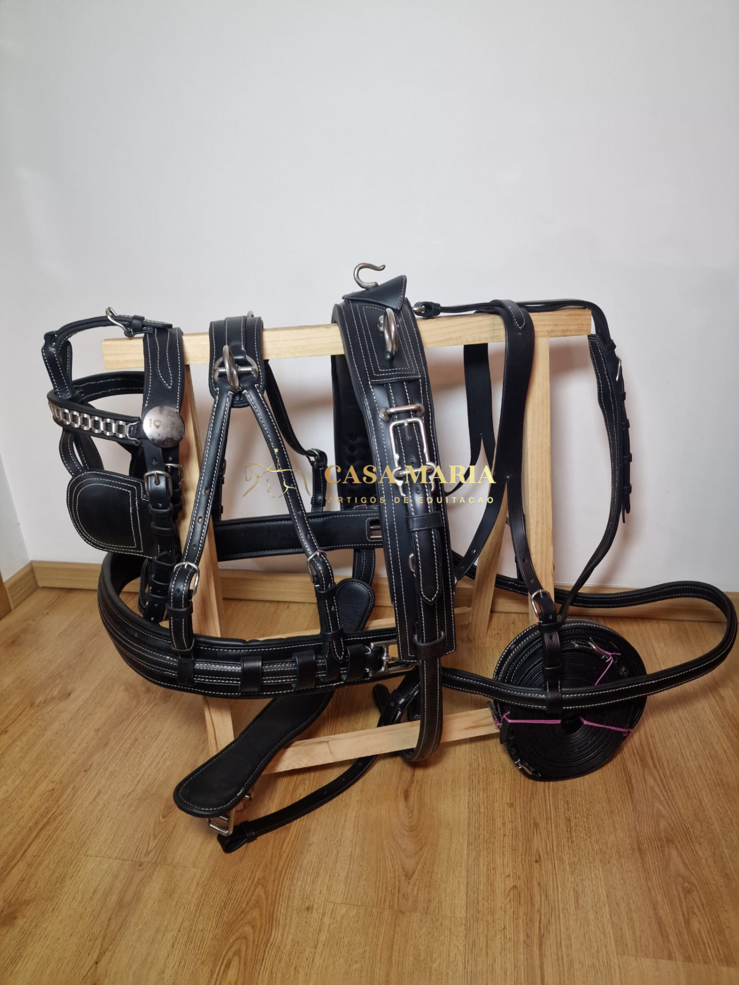 Equipamento equestre de couro preto pendurado em suporte de madeira