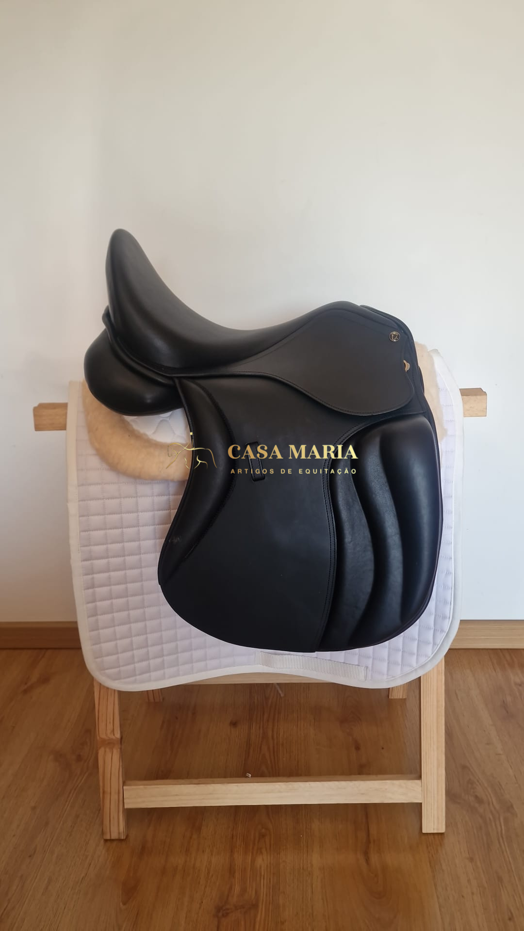 Sela de equitação preta de couro sobre tapete branco acolchoado em suporte de madeira clara