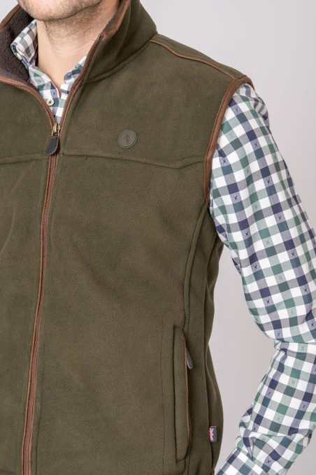 Colete verde oliva em tecido polar com fecho e detalhes castanhos, usado sobre camisa xadrez