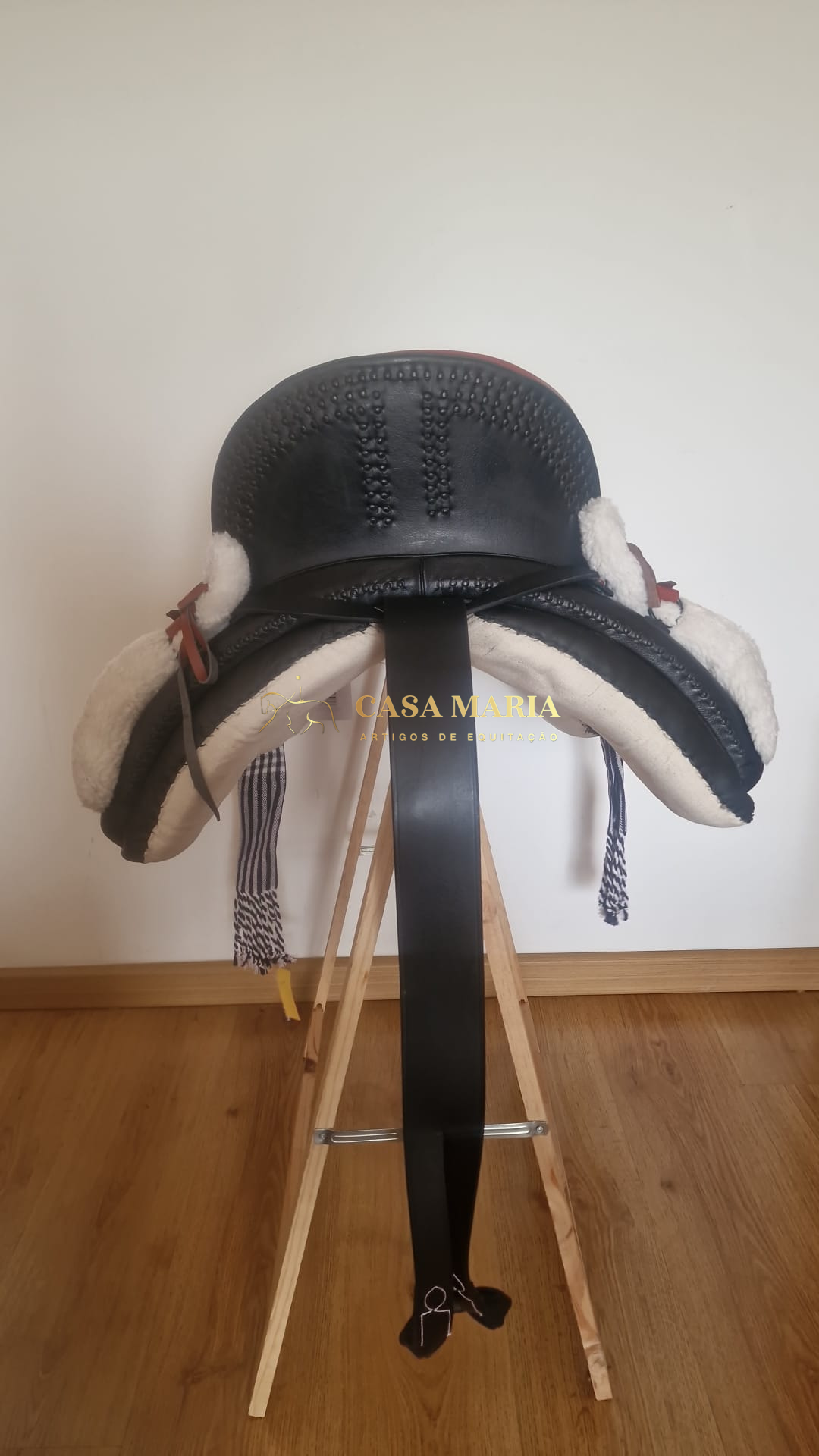 Sela de cavalo preta com acolchoamento branco sobre suporte de madeira