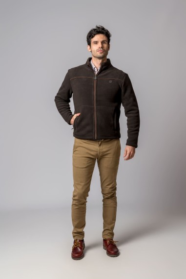 Homem com casaco castanho escuro, calças bege e sapatos castanhos em fundo cinza