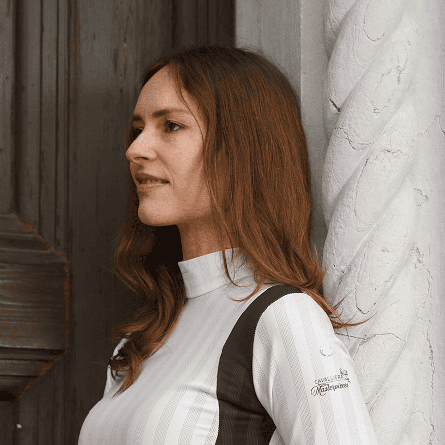 Mulher com jersey desportivo branco e preto, com texto no braço direito, encostada a parede branca.