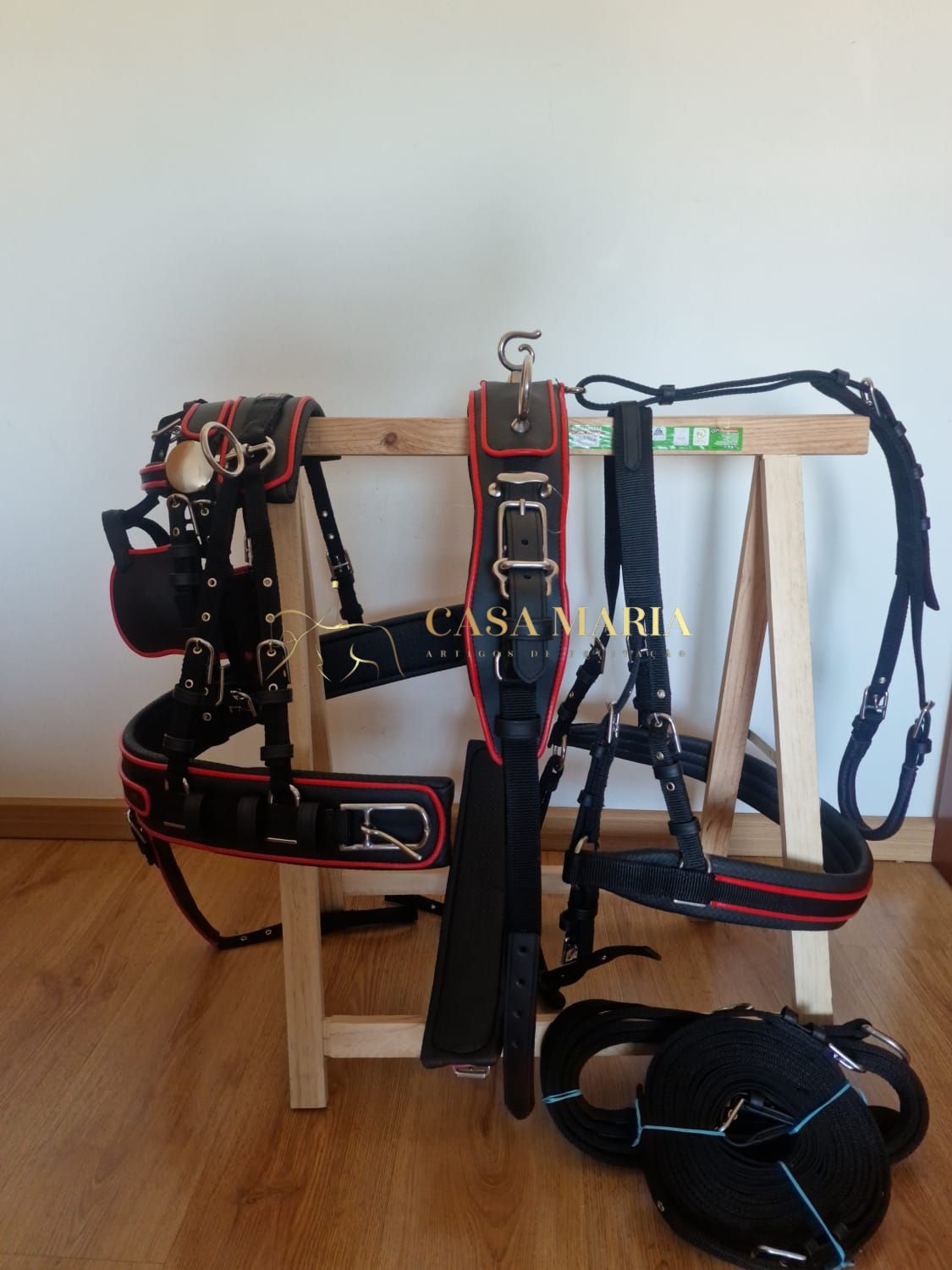 Set de arreios para equitação preto com detalhes vermelhos pendurado em suporte de madeira