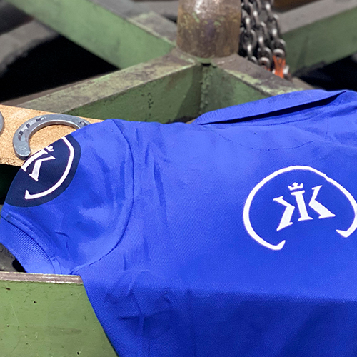 T-shirt azul com logos brancos de KK numa estrutura metálica verde
