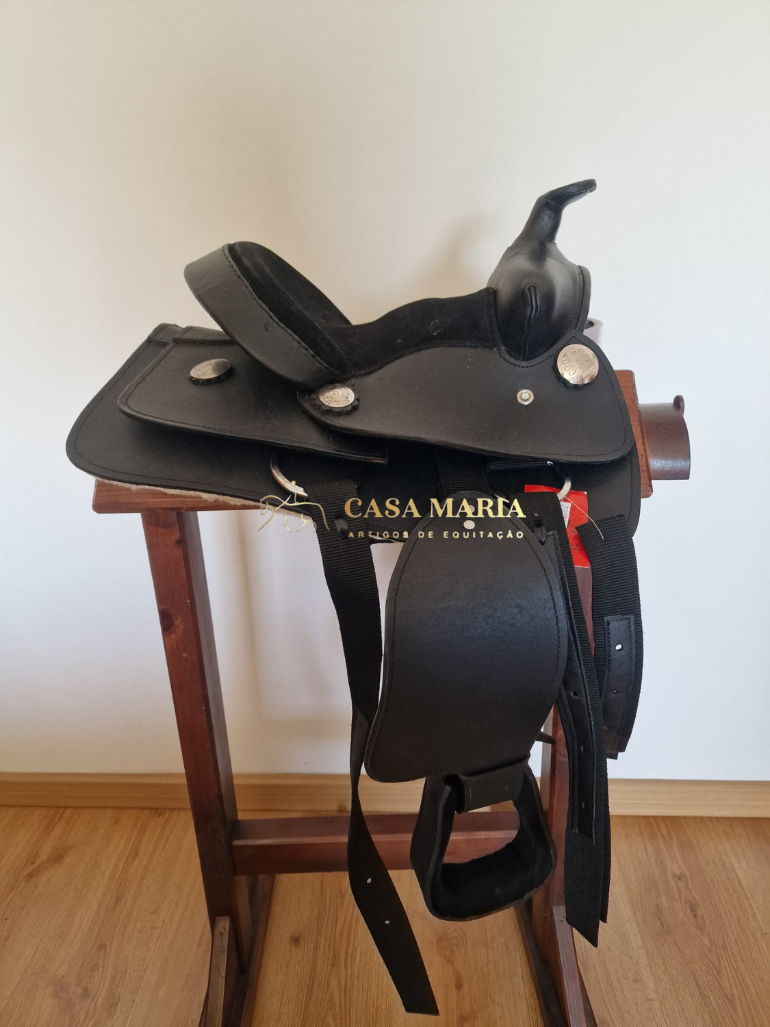 Sela preta de equitação com detalhes em metal em suporte de madeira