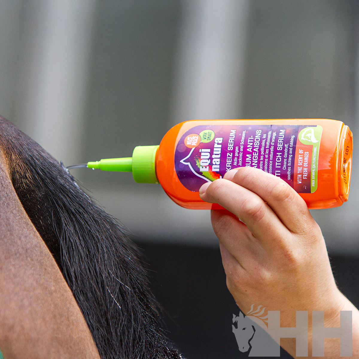 Frasco laranja com tampa verde sendo aplicado na crina de um cavalo castanho