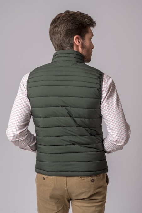 Colete acolchoado verde escuro visto de costas, usado com camisa xadrez e calças cáqui