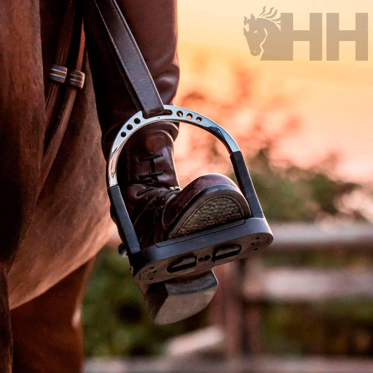 Pé de cavaleiro com bota e estribo metálico em cavalo castanho ao pôr do sol