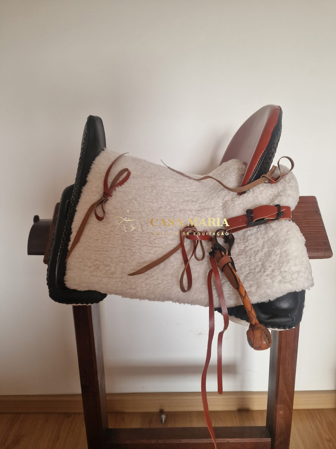 Selim de equitação em madeira com almofada branca e correias castanhas num suporte de madeira