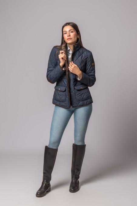Mulher de pé com casaco acolchoado azul escuro, jeans e botas castanhas altas