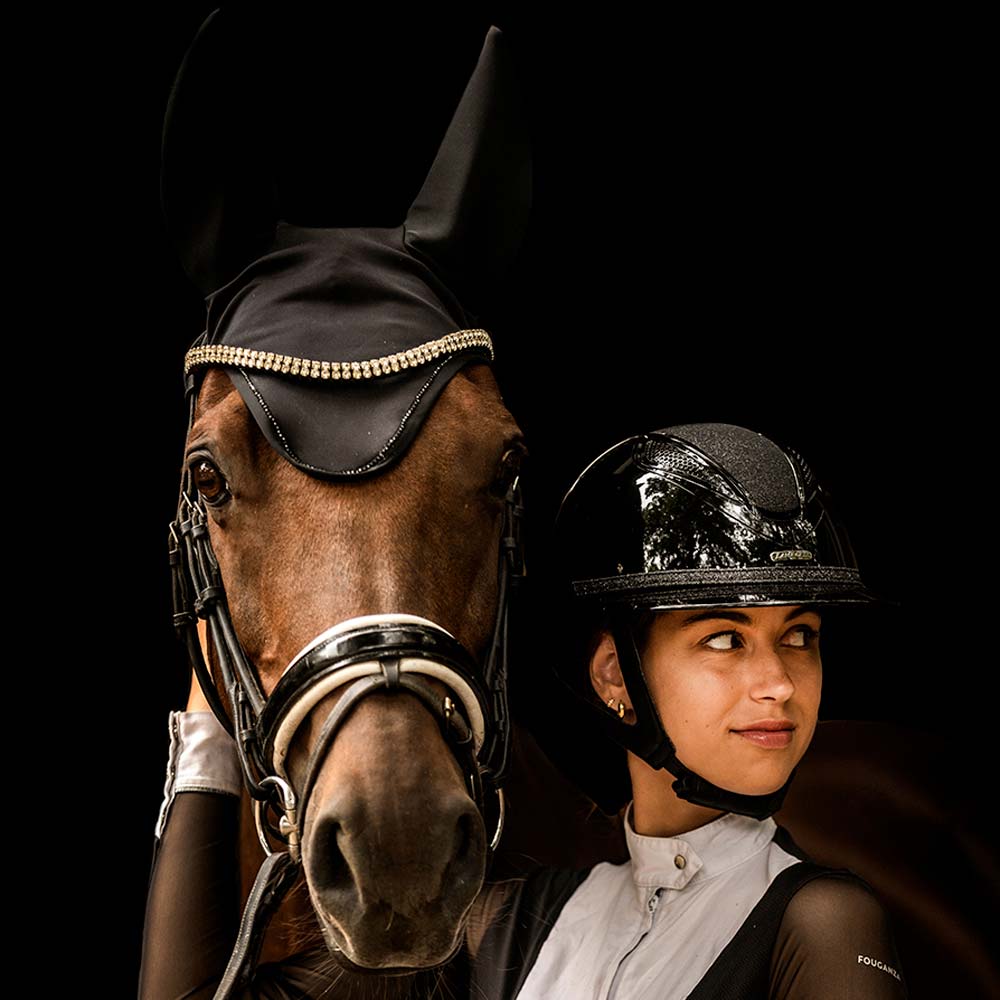 Cavalo castanho com touca preta com strass e mulher com capacete preto e roupa de equitação