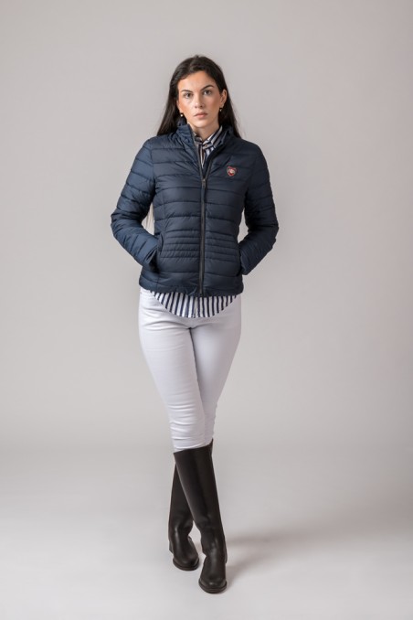 Mulher vestindo casaco acolchoado azul-marinho, camisa riscada azul e branca, calças brancas e botas pretas