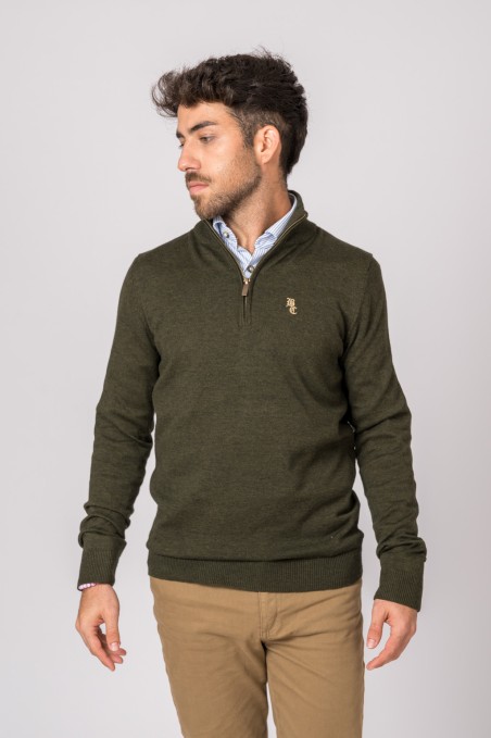 Homem com camisola de malha verde-oliva com fecho curto e logótipo bordado, camisa azul e calças bege