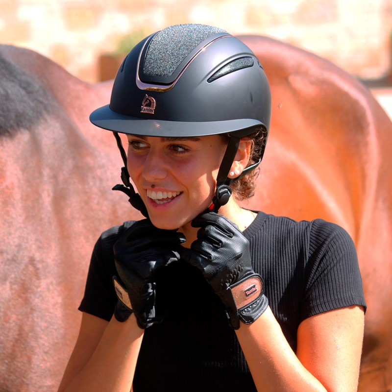 Mulher com capacete de equitação preto e luvas de couro ao lado de cavalo castanho