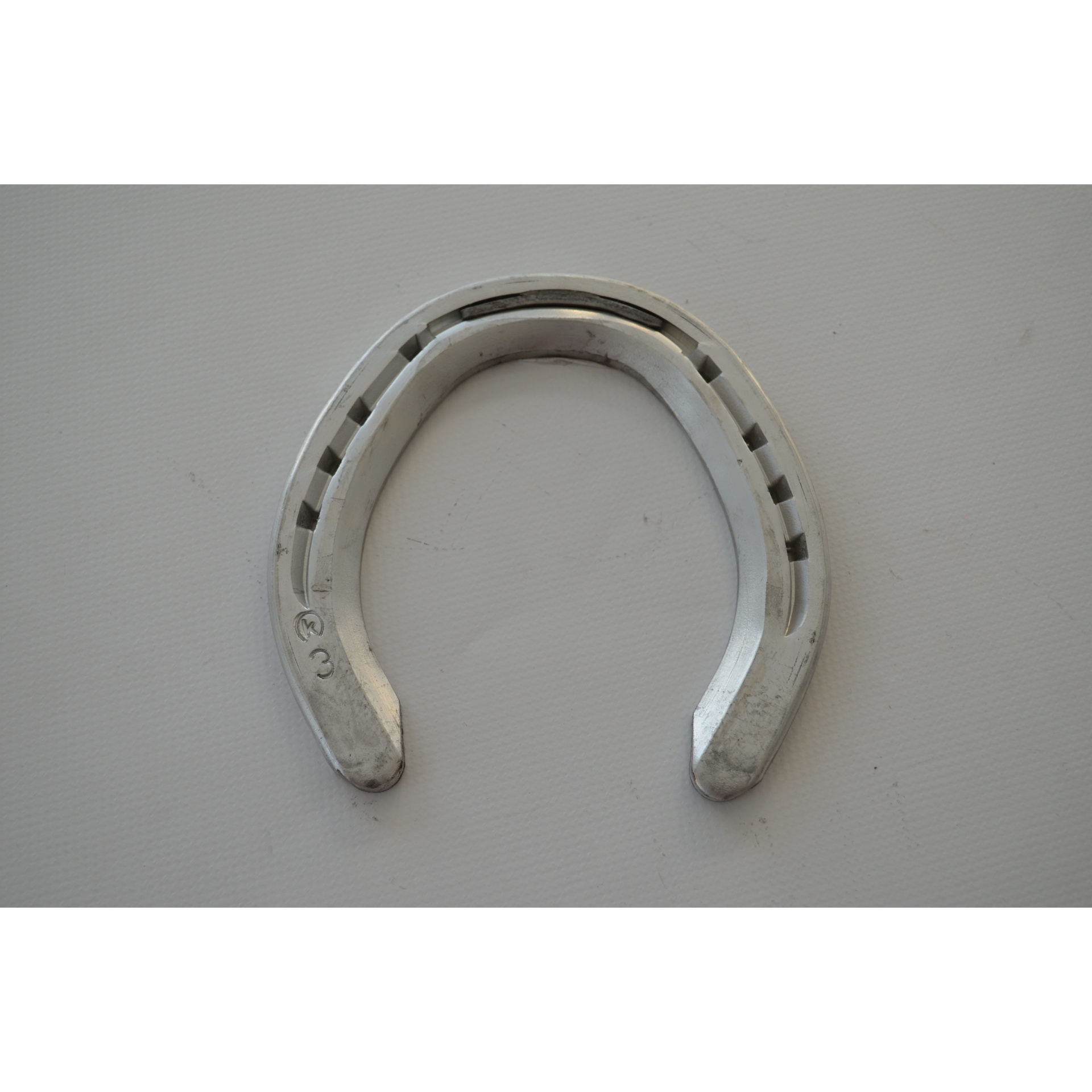 Ferradura metálica prateada com furos sobre fundo branco