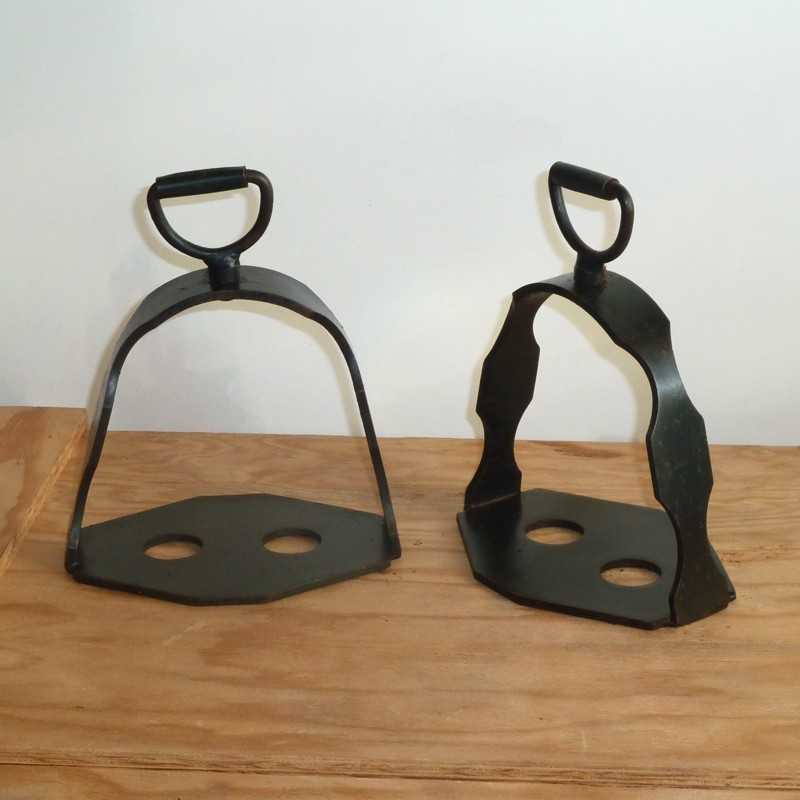 Par de estribos metálicos pretos com punhos em D sobre superfície de madeira
