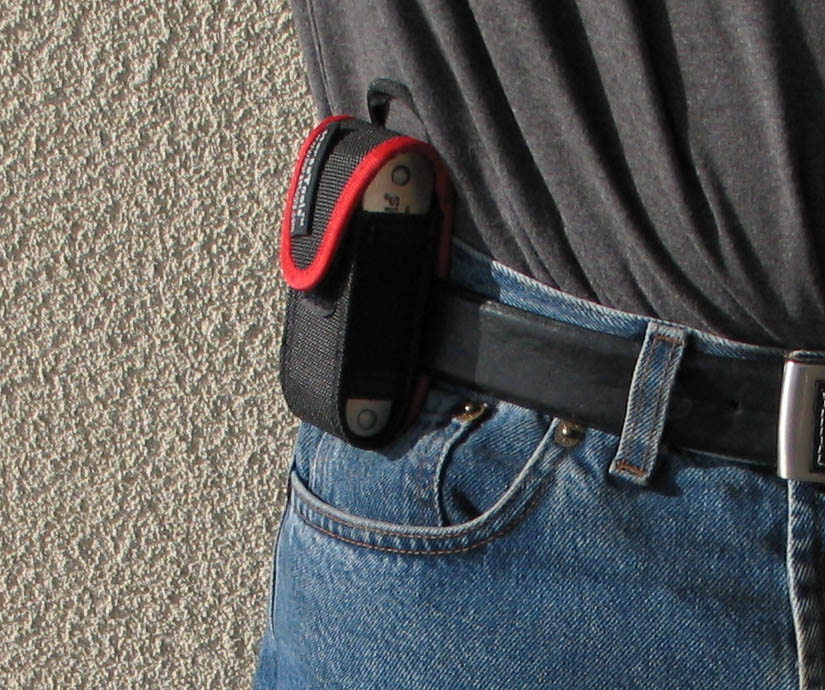 Capa preta e vermelha presa a um cinto em calças de ganga azuis