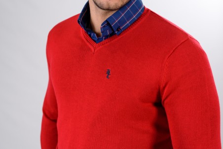 Camisola vermelha com decote em V e logótipo azul, sobre camisa azul xadrez.