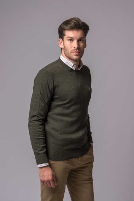 Homem com camisola verde escura, camisa xadrez branca e calças castanho claro