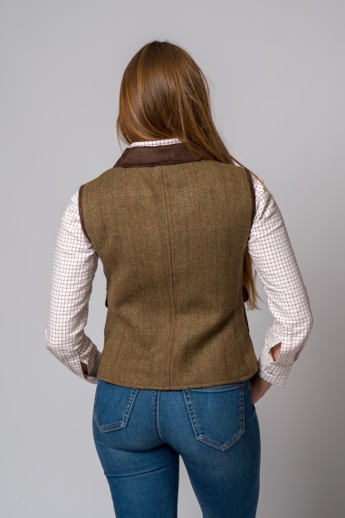 Mulher de costas a usar colete castanho tweed com gola escura, camisa branca xadrez e calças de ganga azul.