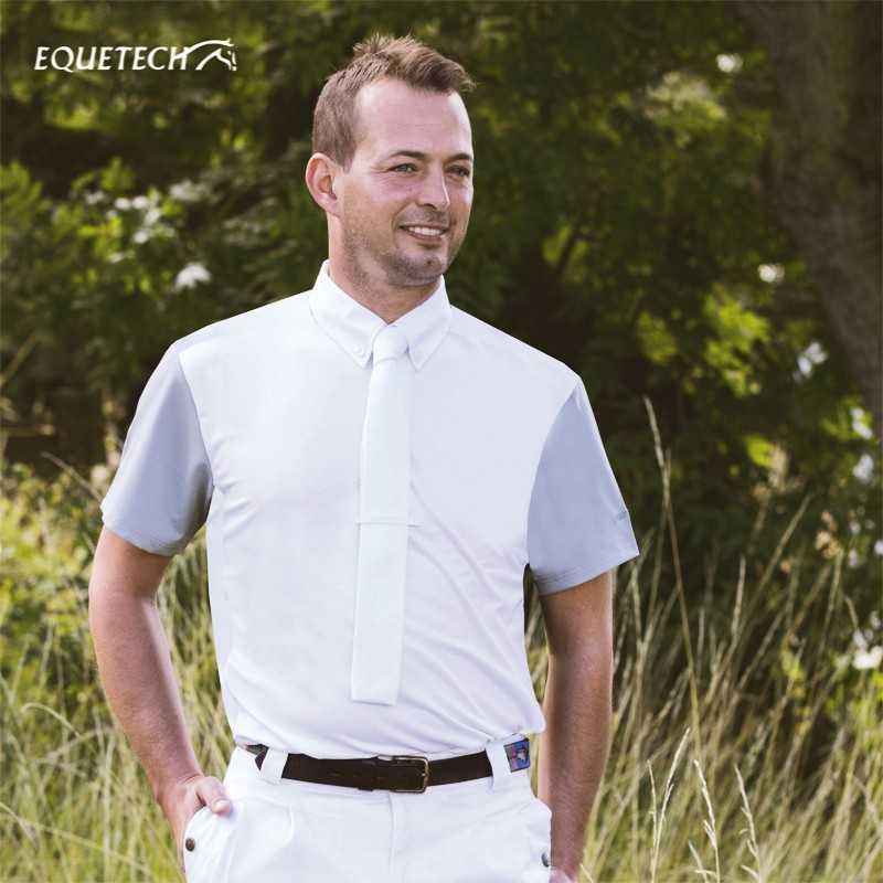 Homem com camisa branca e detalhes cinzentos ao ar livre, próximo a vegetação