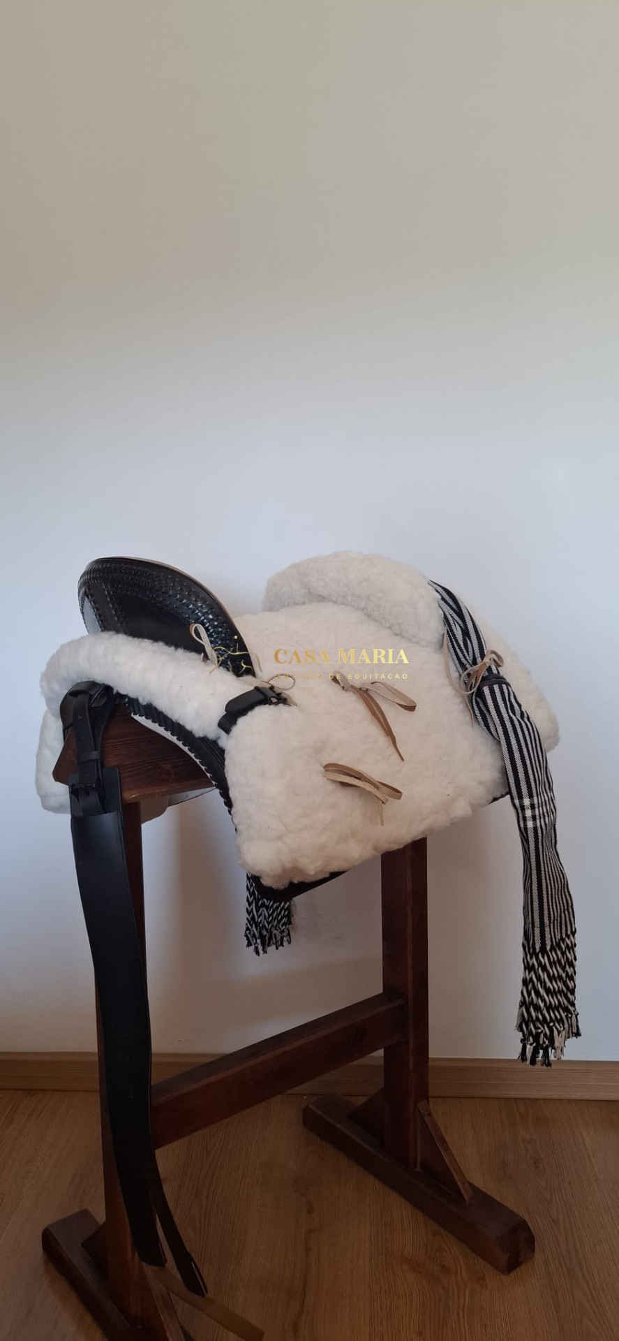 Sela de equitação preta com almofadado branco sobre suporte de madeira