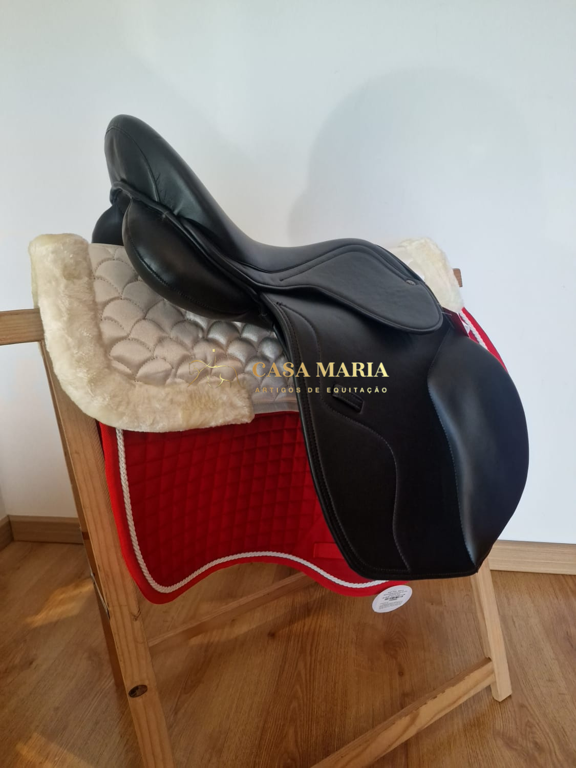 Sela de equitação preta com manta vermelha e almofada creme em suporte de madeira