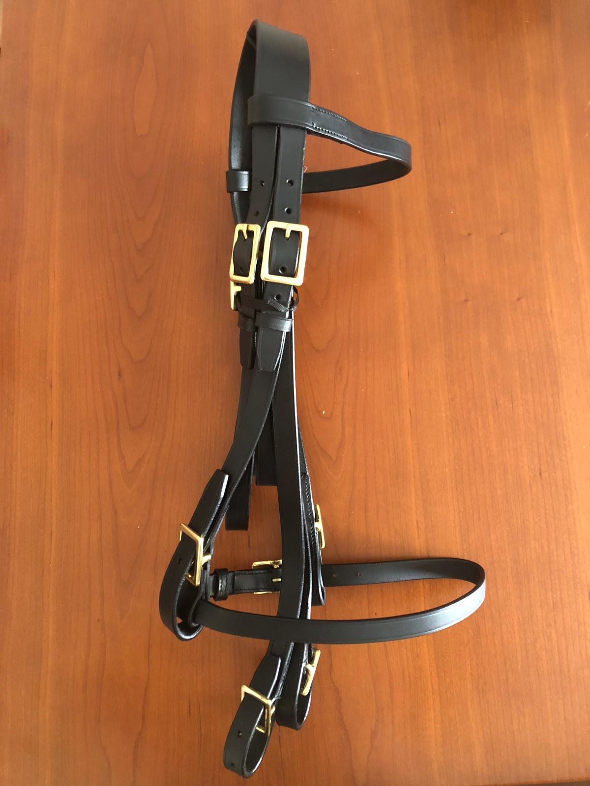 Bridão de couro preto com fivelas douradas numa mesa de madeira clara