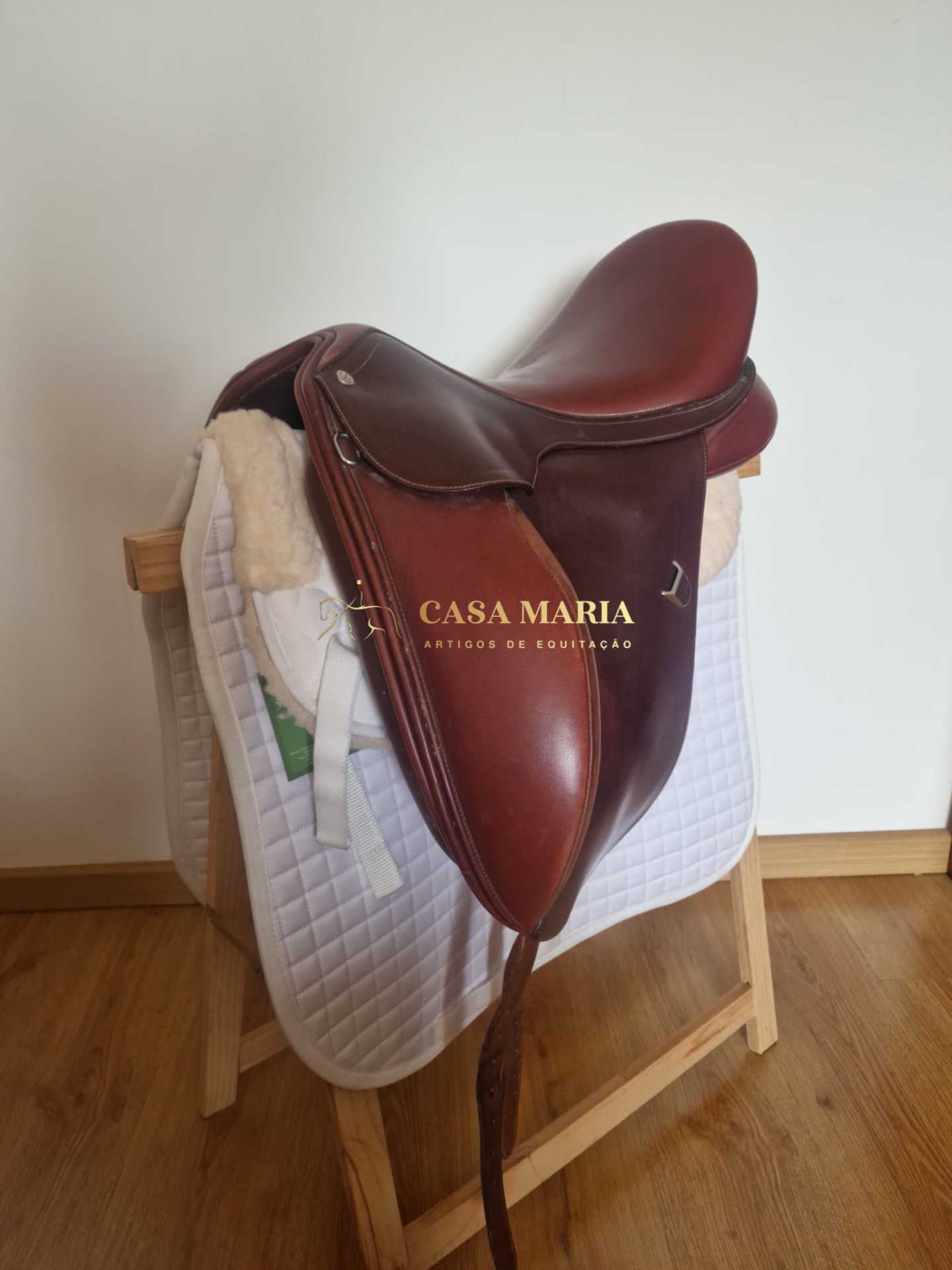 Sela de equitação em couro castanho com almofada branca sobre suporte de madeira