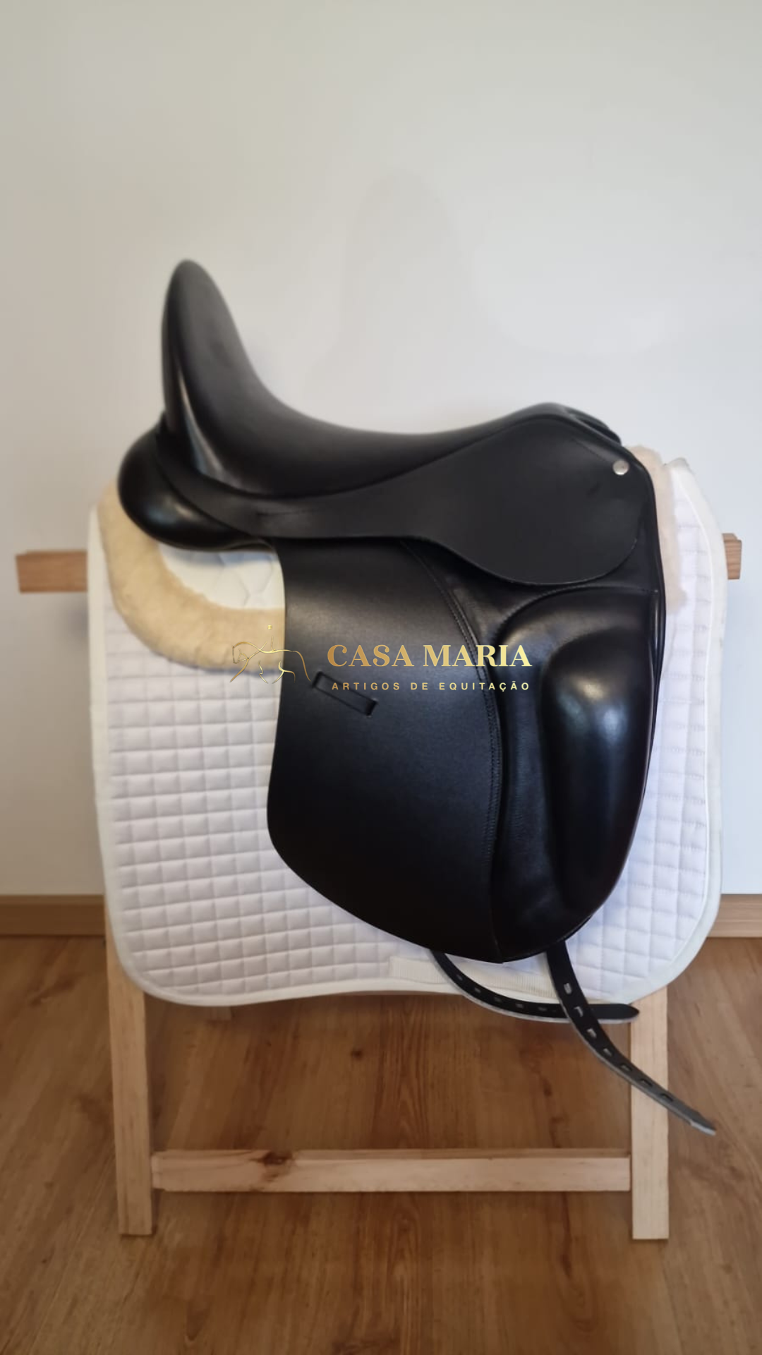 Sela de cavalo preta em couro sobre manta branca acolchoada em estrutura de madeira