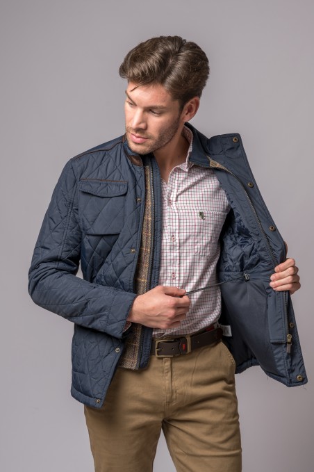 Homem com casaco azul acolchoado aberto mostrando camisa branca xadrez e calças beges