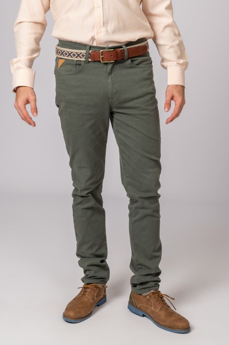 Homem com camisa bege, calças verdes, cinto castanho com faixa estampada e sapatos castanhos com sola azul