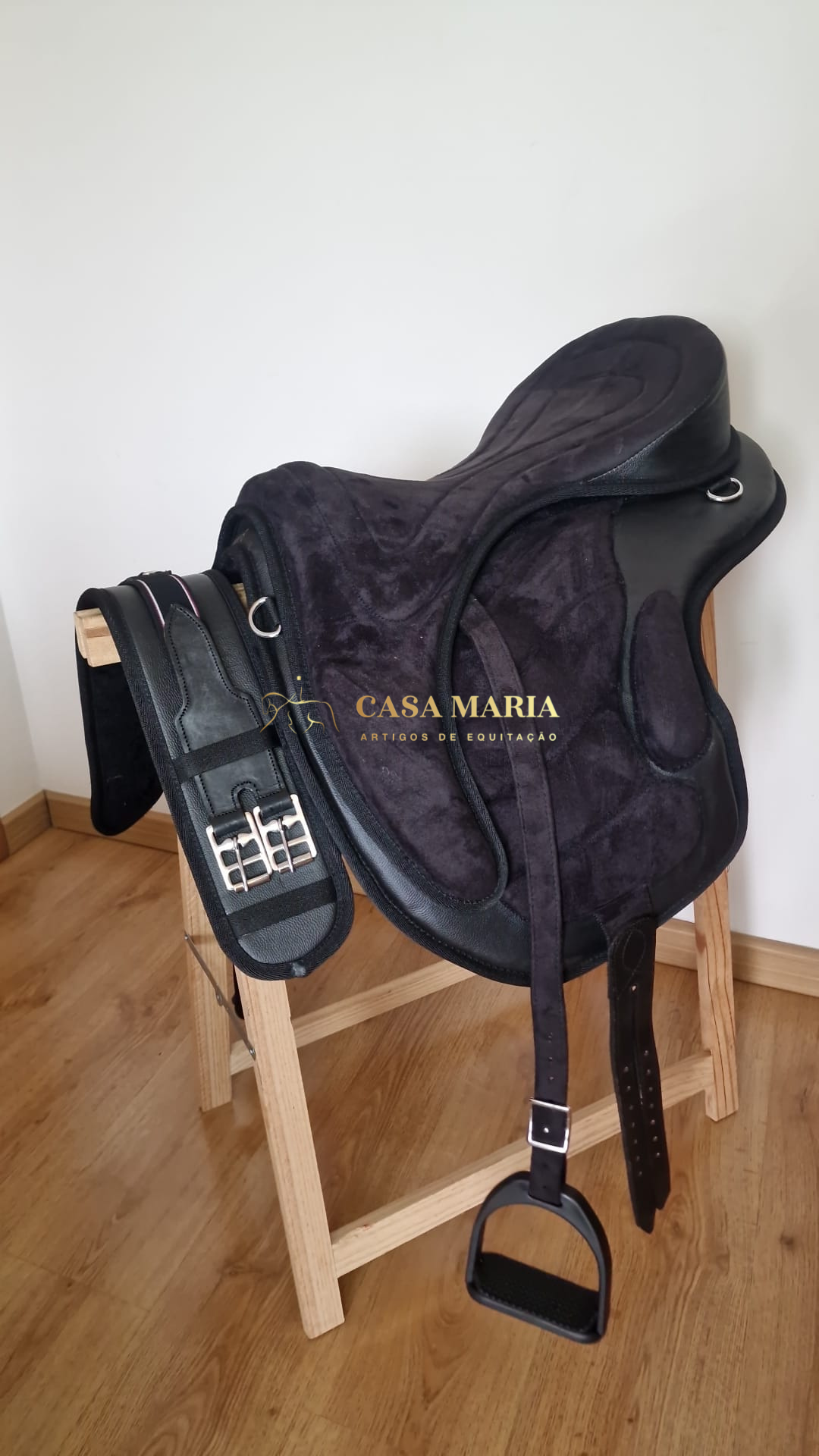 Sela preta de equitação com acessórios sobre suporte de madeira