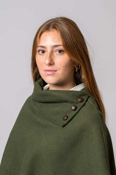 Mulher com capa verde com botões sobre camisa xadrez cinzenta em fundo cinza