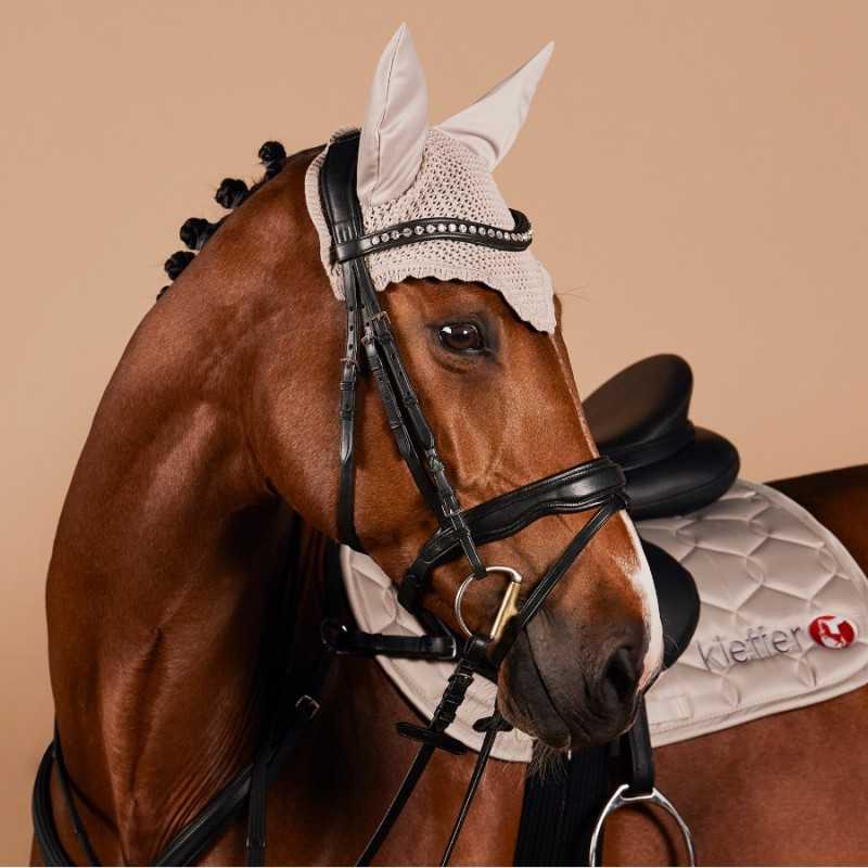 Cavalo castanho com equipamento de equitação incluindo touca bege, selim preto e manta branca com logótipo Kieffer