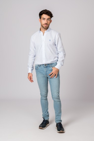 Homem com camisa branca de padrão azul e jeans claros, em fundo cinzento claro.