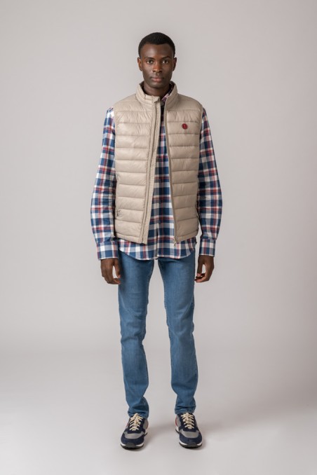 Homem com colete acolchoado bege e camisa xadrez azul, vermelho e branco com jeans azul