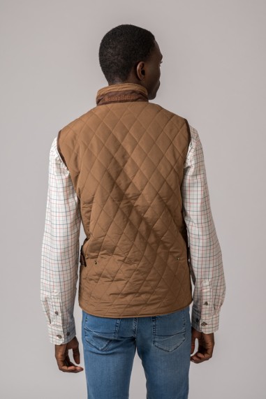 Colete acolchoado castanho com padrão de losangos e gola alta com texto, camisa xadrez branca e calças de ganga azuis de costas.