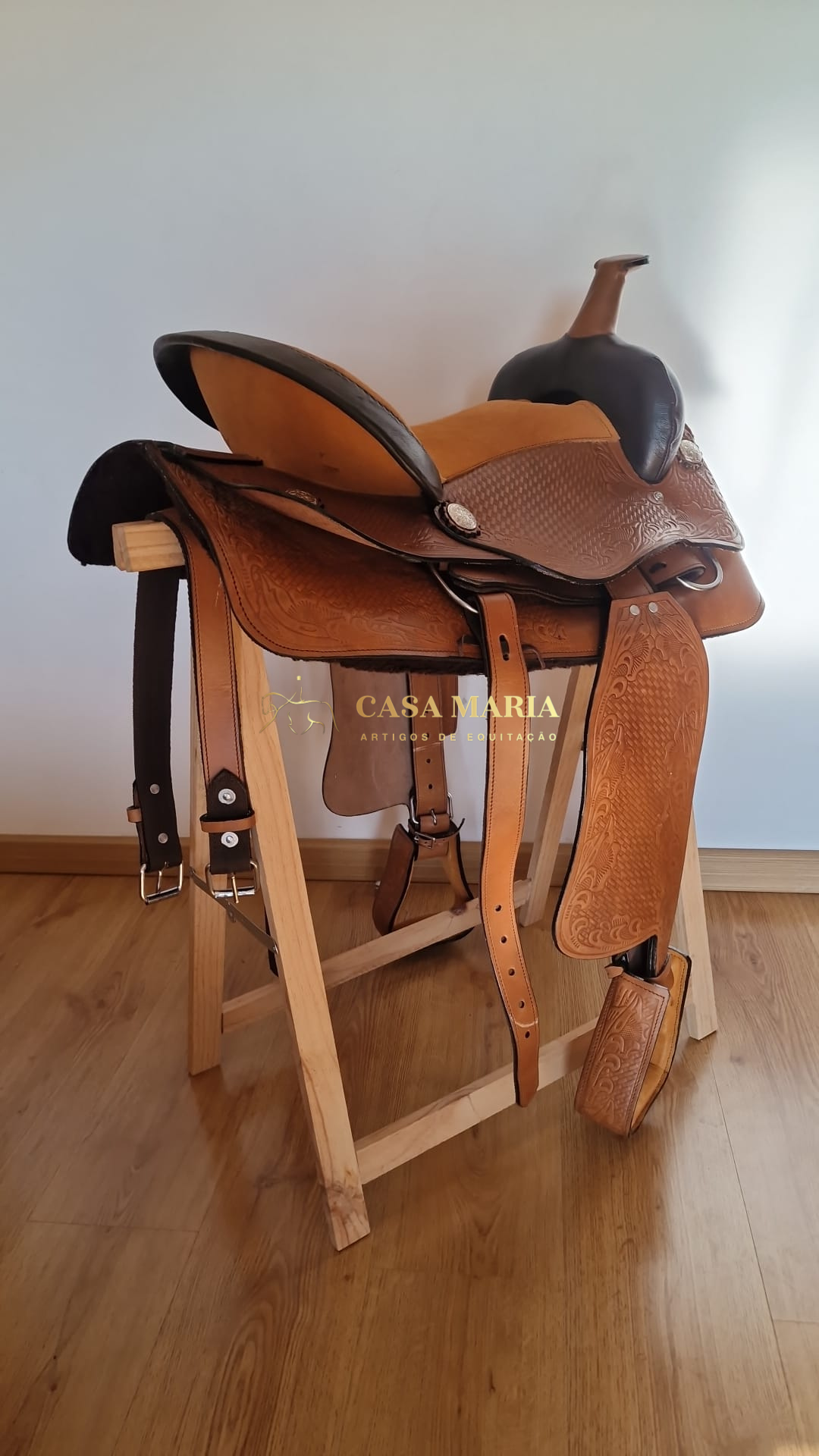 Sela de equitação em couro castanho com assento preto num suporte de madeira