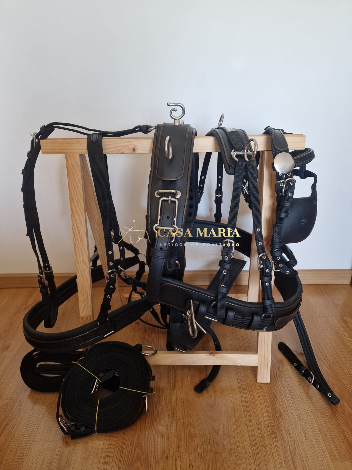 Acessórios para equitação em sintético preto pendurados num suporte de madeira clara