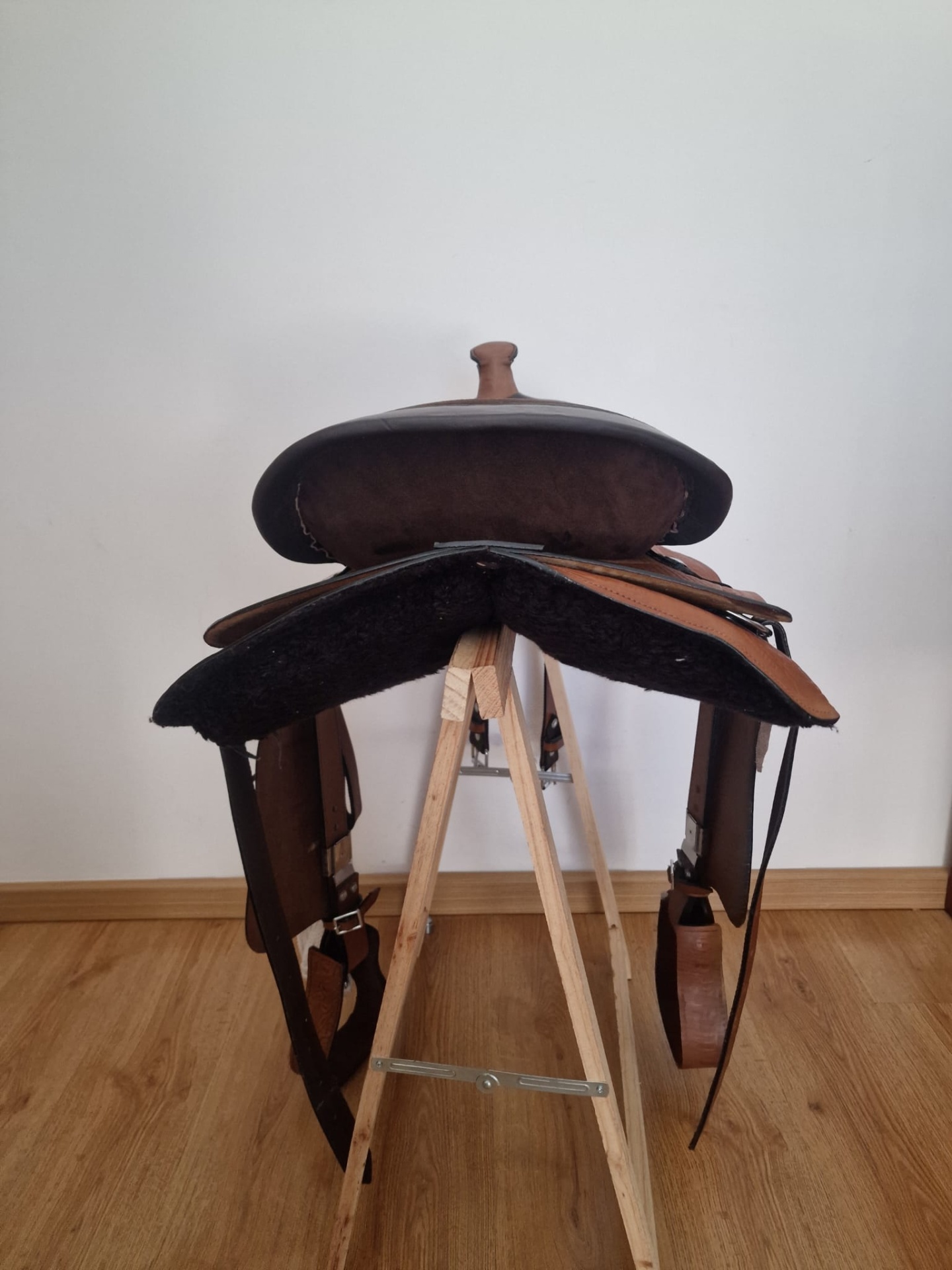 Sela de equitação em couro castanho sobre suporte de madeira
