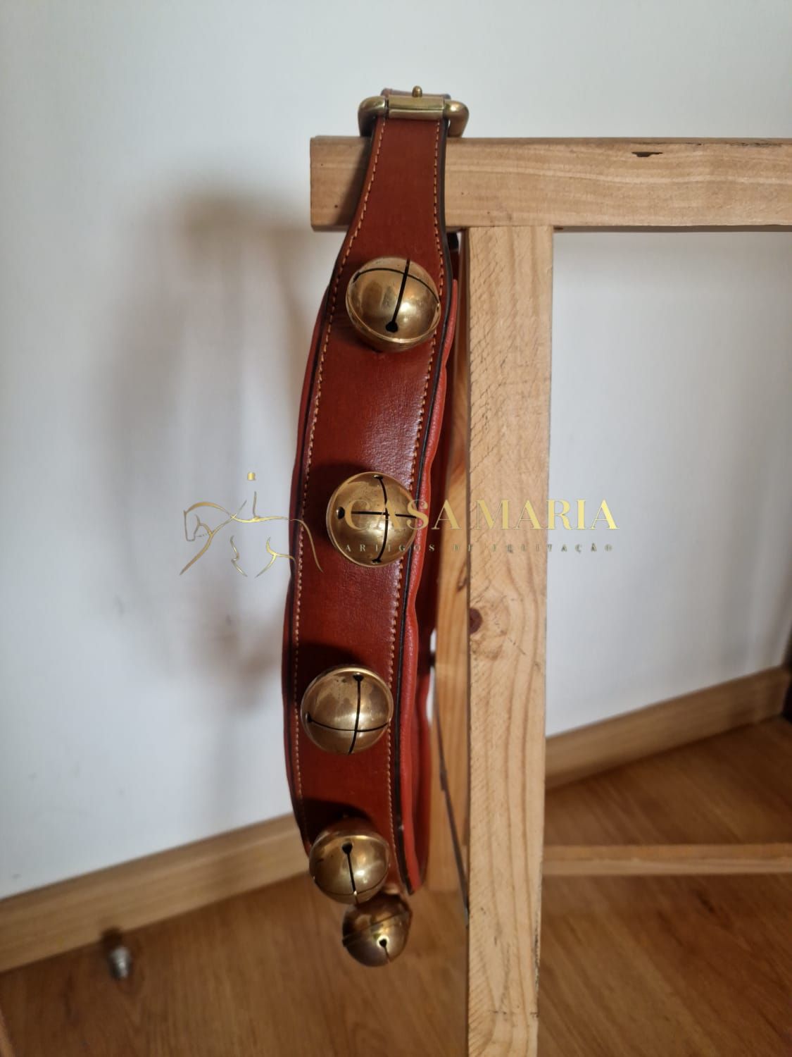 Cinto em pele castanha com guizos dourados pendurado numa cadeira de madeira