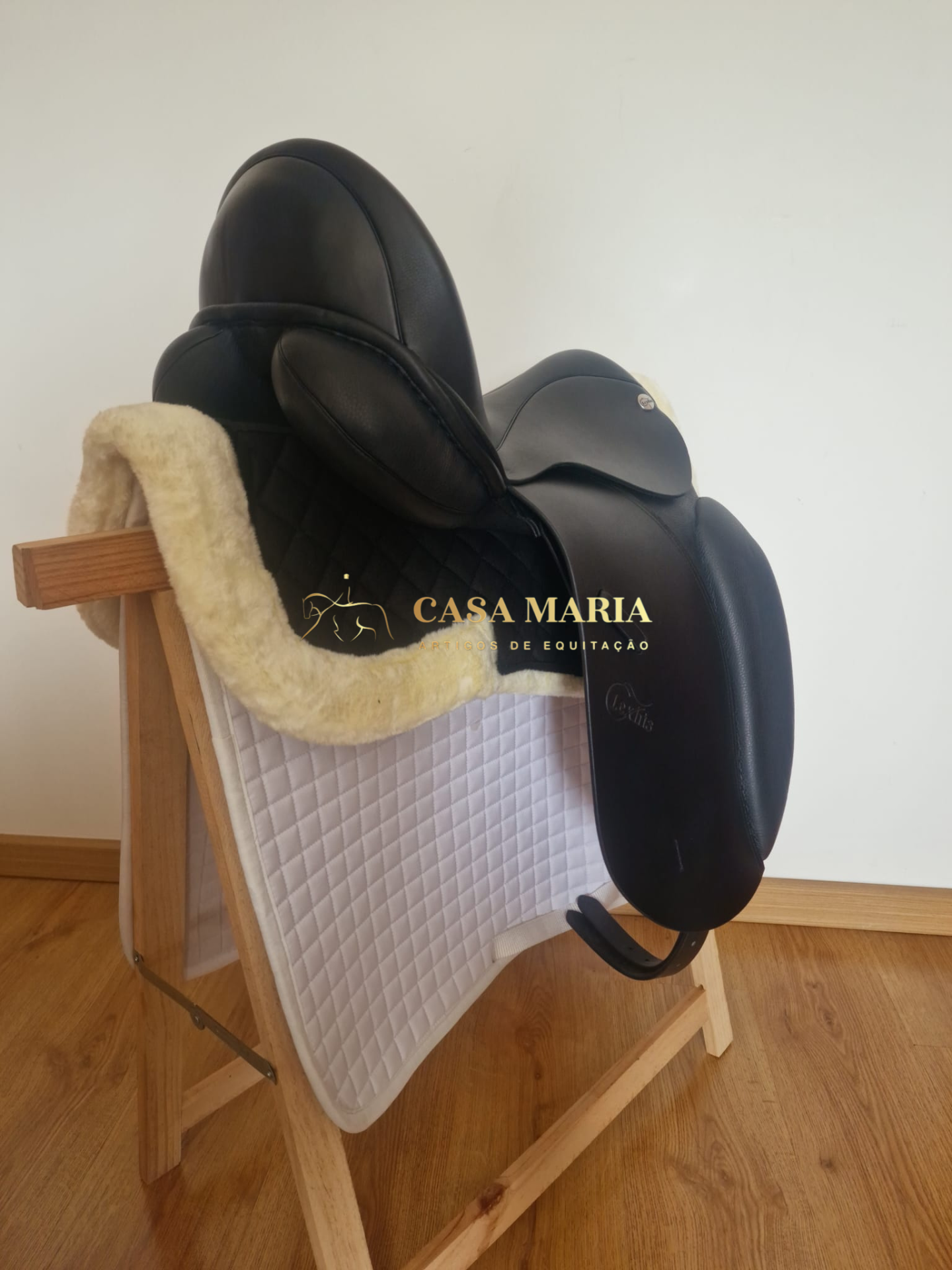 Sela de equitação preta sobre suporte de madeira com manta branca acolchoada