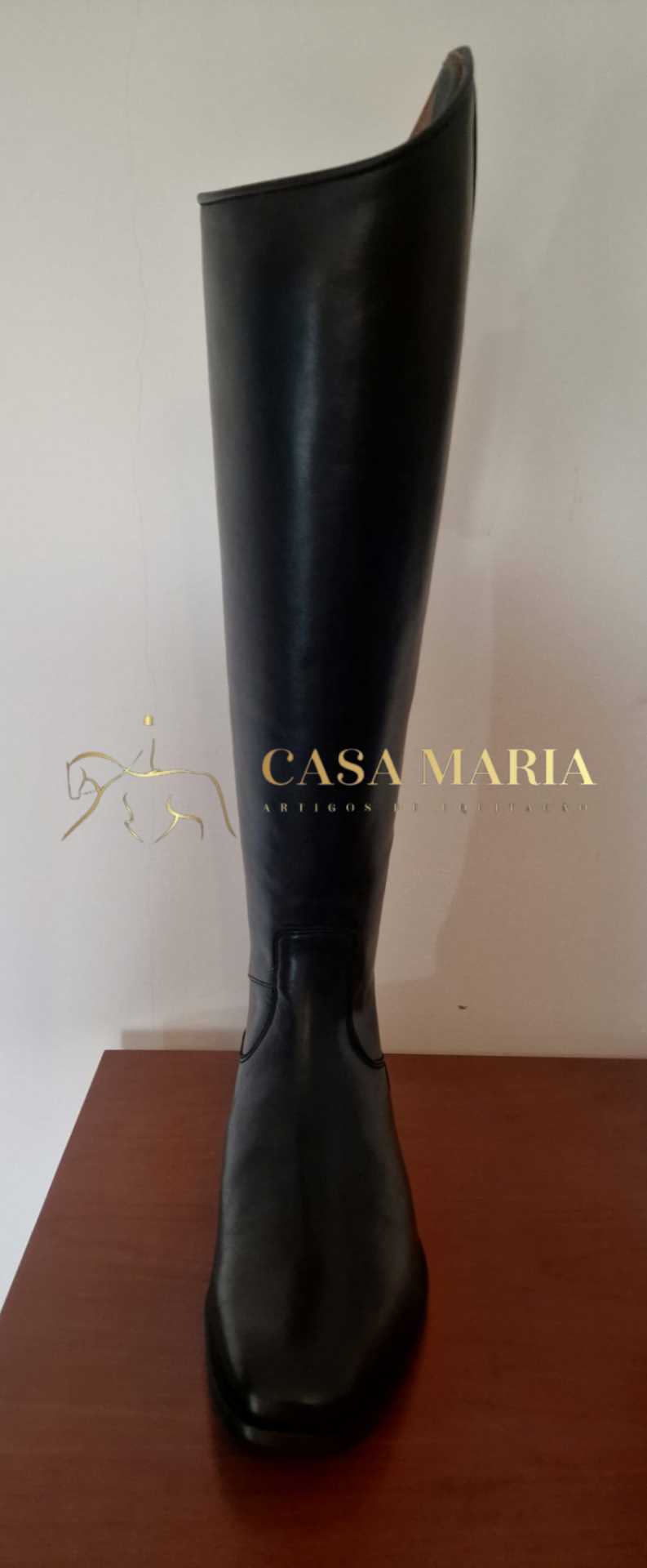 Bota alta preta de couro com bico quadrado sobre superfície de madeira