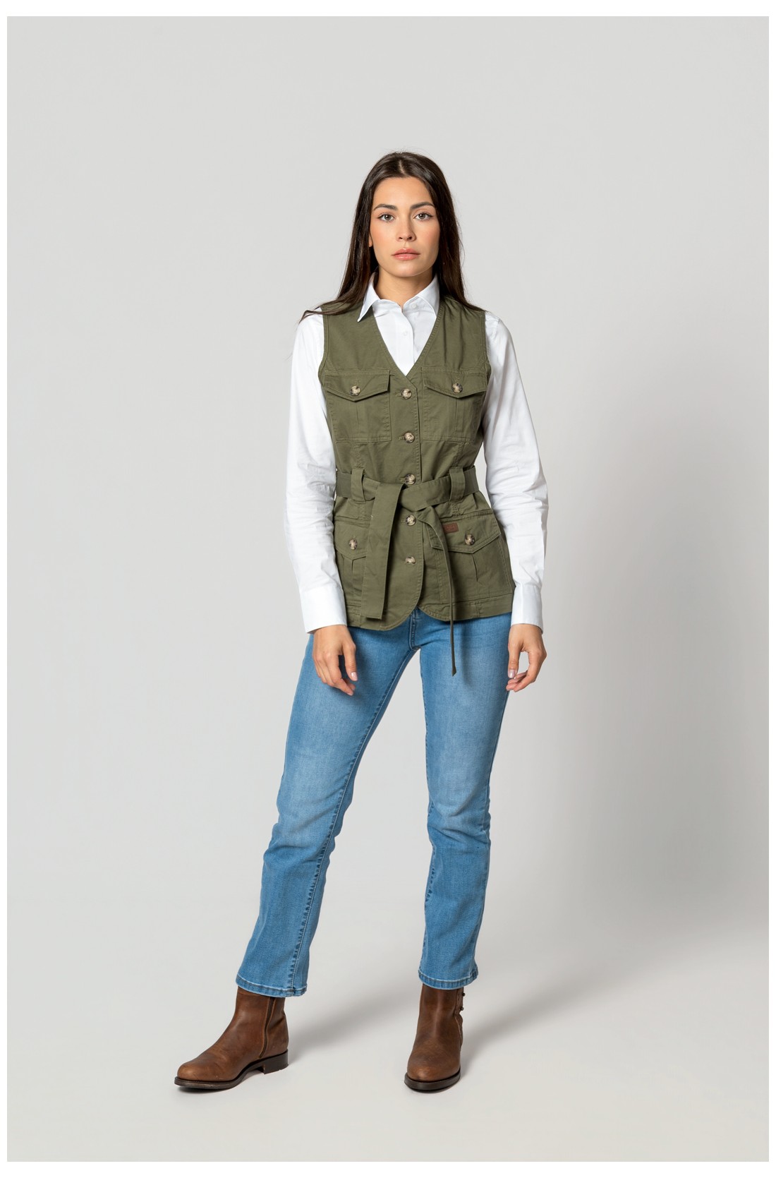 Mulher com colete verde, camisa branca, jeans azul e botas castanhas