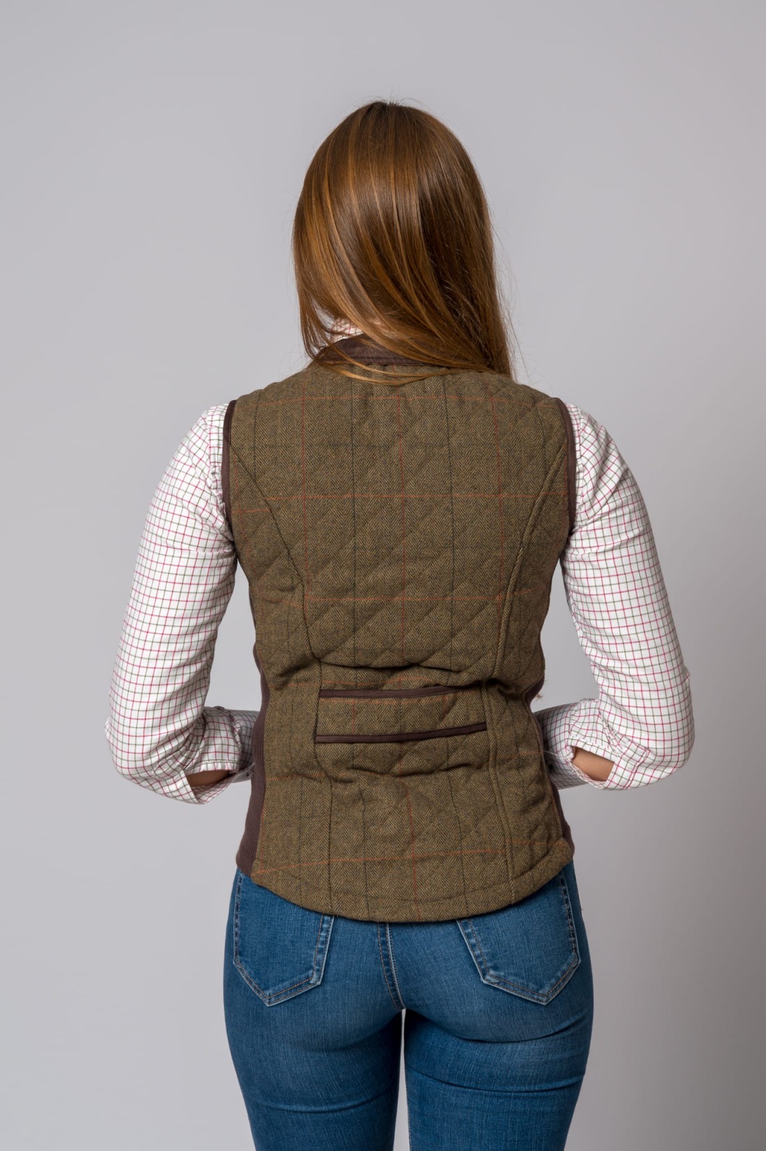 Pessoa de costas a usar colete castanho padrão tweed e camisa xadrez com calças de ganga azuis