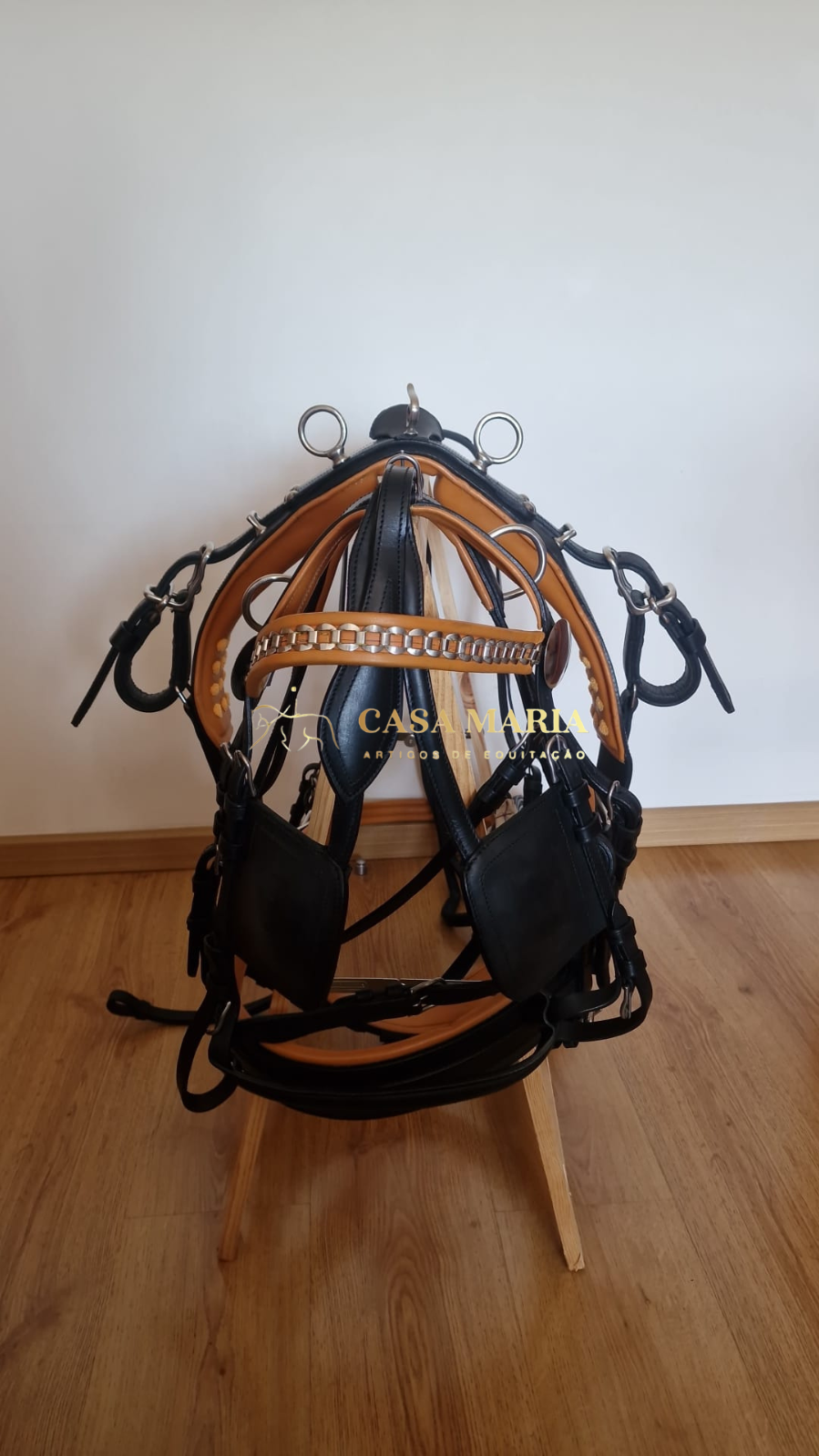 Cabeçada e arreio de couro preto e castanho com ferragens metálicas num suporte de madeira
