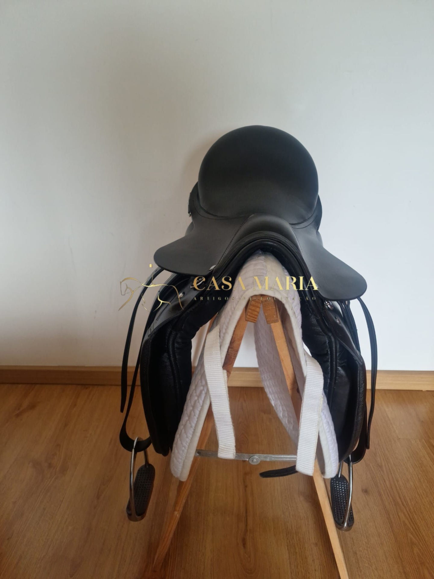 Sela de equitação preta em couro num suporte de madeira com manta branca.